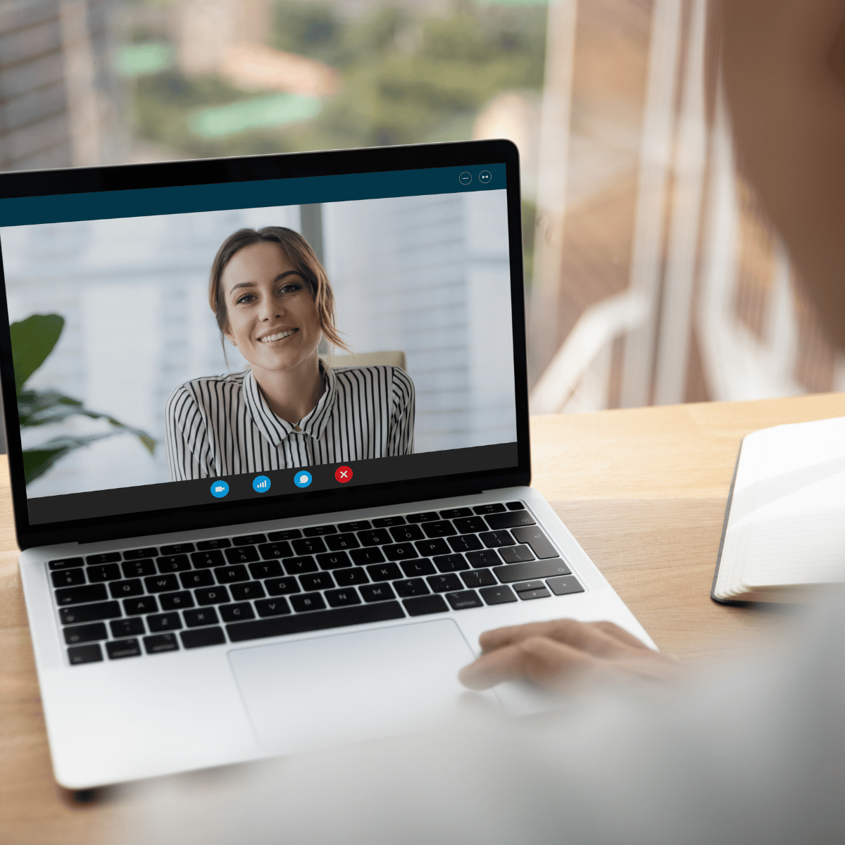 Laptop showing a smiling woman in a striped shirt during a video call on a wooden desk.